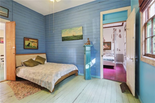 bedroom featuring wooden walls, light hardwood / wood-style flooring, and ceiling fan