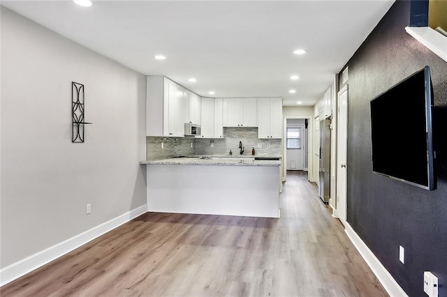 kitchen featuring white cabinetry, light stone counters, backsplash, kitchen peninsula, and light wood-type flooring