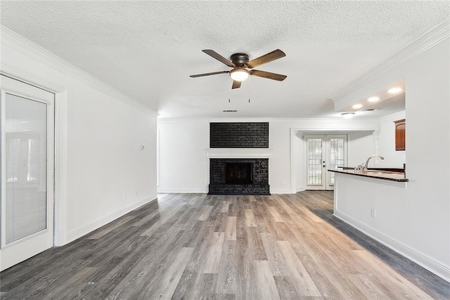 unfurnished living room featuring ornamental molding, a brick fireplace, a textured ceiling, light hardwood / wood-style floors, and ceiling fan