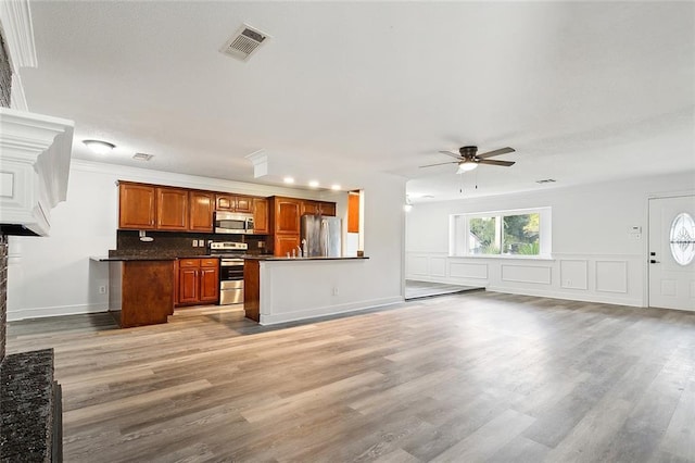 kitchen with a stone fireplace, ceiling fan, light wood-type flooring, appliances with stainless steel finishes, and tasteful backsplash