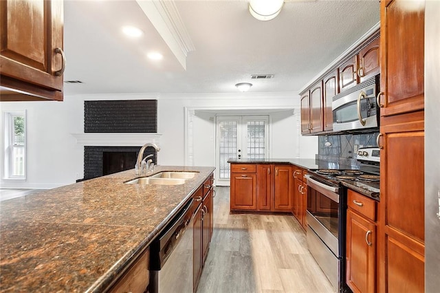 kitchen with appliances with stainless steel finishes, sink, a fireplace, ornamental molding, and light hardwood / wood-style flooring