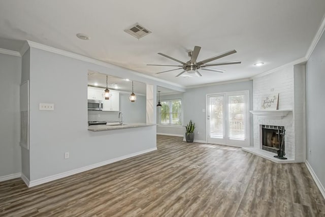 unfurnished living room featuring a fireplace, wood-type flooring, ceiling fan, and crown molding