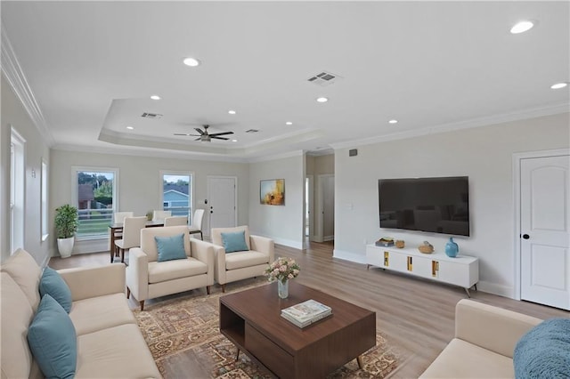 living room featuring ceiling fan, a tray ceiling, ornamental molding, and light hardwood / wood-style flooring