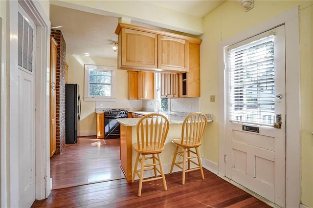 kitchen with black stove, decorative backsplash, stainless steel fridge, a kitchen bar, and kitchen peninsula