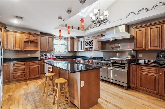 kitchen featuring a center island, pendant lighting, appliances with stainless steel finishes, brown cabinetry, and wall chimney exhaust hood