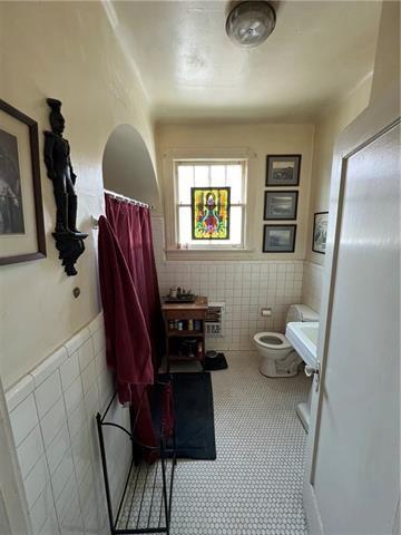 bathroom with toilet and tile walls