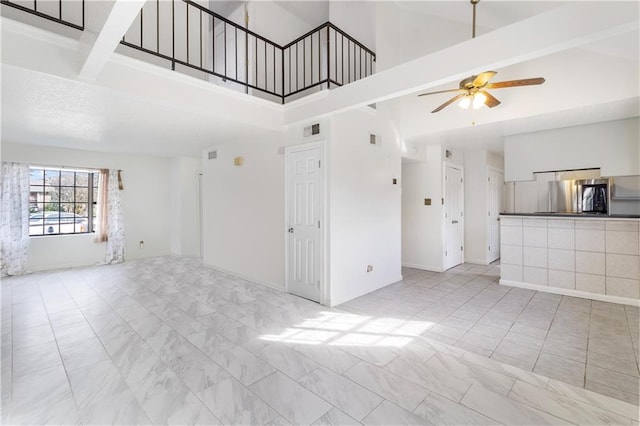 unfurnished living room featuring beam ceiling, a towering ceiling, and ceiling fan