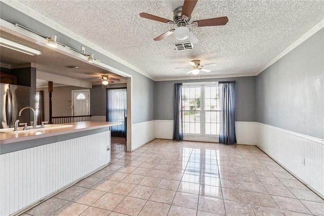 kitchen with sink, ornamental molding, a textured ceiling, light tile patterned flooring, and stainless steel refrigerator