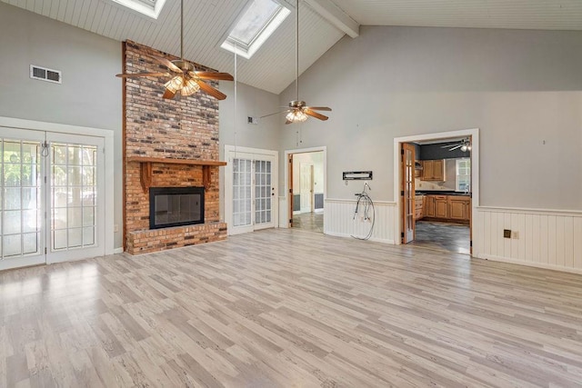 unfurnished living room with light hardwood / wood-style floors, a skylight, high vaulted ceiling, and a fireplace