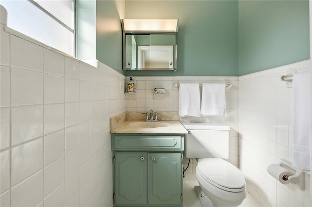 bathroom featuring toilet, vanity, and tile walls