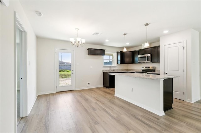 kitchen featuring stainless steel appliances, a center island, decorative light fixtures, light stone counters, and light hardwood / wood-style floors