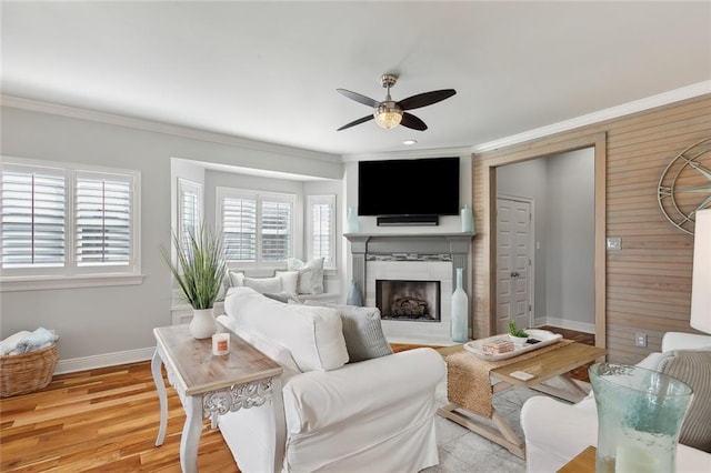 living room with ceiling fan, ornamental molding, a tile fireplace, and light hardwood / wood-style flooring