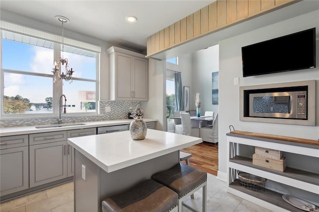 kitchen with a breakfast bar, sink, decorative backsplash, gray cabinets, and a notable chandelier