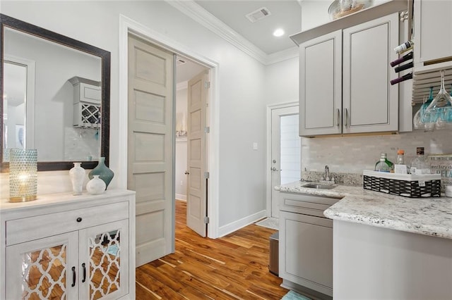 kitchen with sink, light stone counters, backsplash, light hardwood / wood-style floors, and ornamental molding