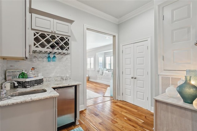 bar featuring light stone countertops, sink, stainless steel dishwasher, light wood-type flooring, and ornamental molding