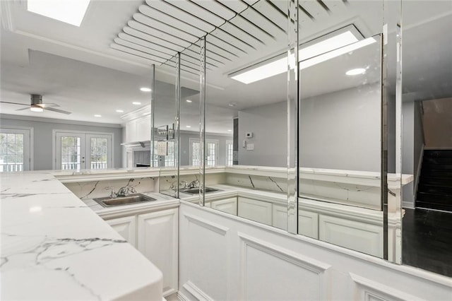 kitchen featuring white cabinetry, ceiling fan, light stone counters, and a sink