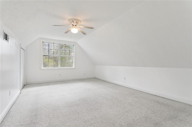 additional living space featuring light carpet, a textured ceiling, lofted ceiling, and ceiling fan