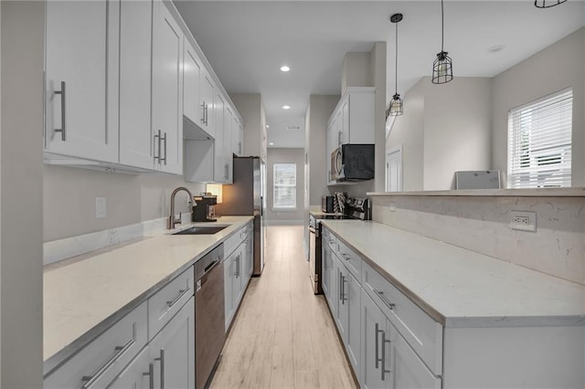 kitchen with sink, pendant lighting, white cabinetry, appliances with stainless steel finishes, and light hardwood / wood-style floors