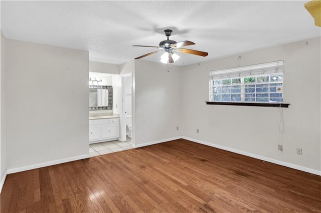 unfurnished bedroom with light hardwood / wood-style floors, a textured ceiling, ensuite bath, and ceiling fan