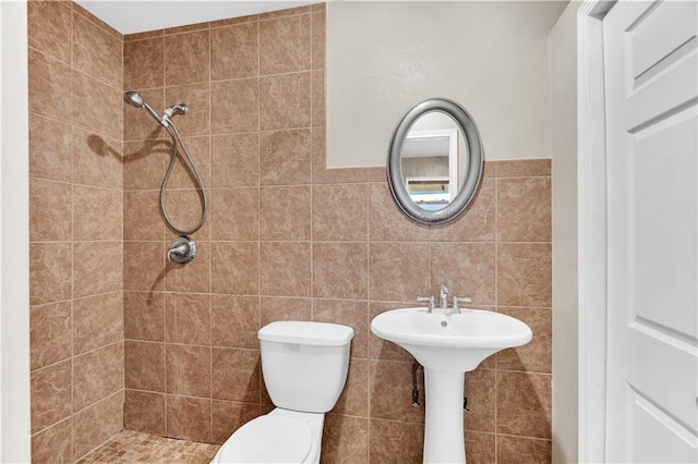 bathroom with a tile shower, toilet, and tile walls