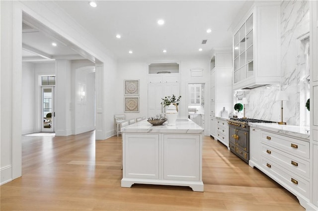 kitchen with a center island, light wood-type flooring, white cabinetry, and stainless steel stove