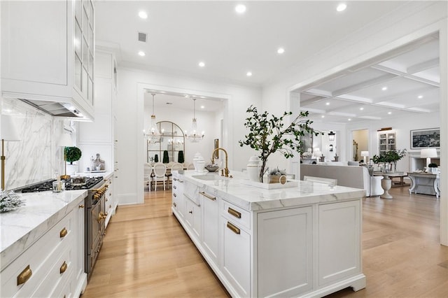 kitchen with a kitchen island with sink, stainless steel range, white cabinets, and light hardwood / wood-style flooring