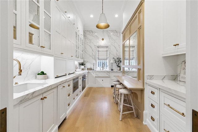 kitchen with backsplash, light stone counters, white cabinets, and decorative light fixtures