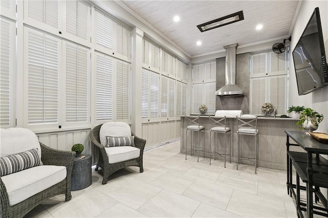 kitchen with a kitchen breakfast bar, wall chimney range hood, crown molding, light tile patterned floors, and kitchen peninsula