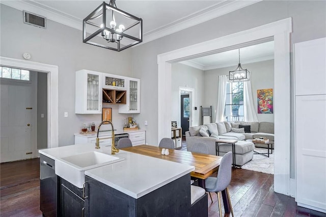 kitchen with a kitchen island with sink, ornamental molding, sink, decorative light fixtures, and dark hardwood / wood-style flooring