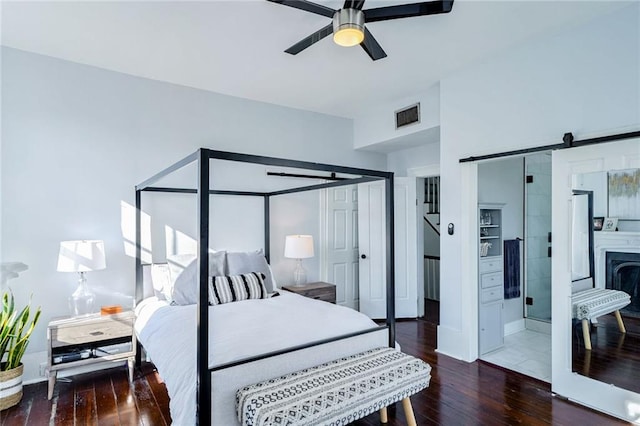 bedroom featuring ensuite bathroom, a barn door, dark wood-type flooring, and ceiling fan