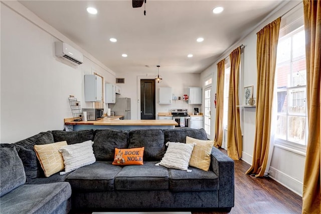 living room featuring a wealth of natural light, a wall mounted AC, and wood-type flooring