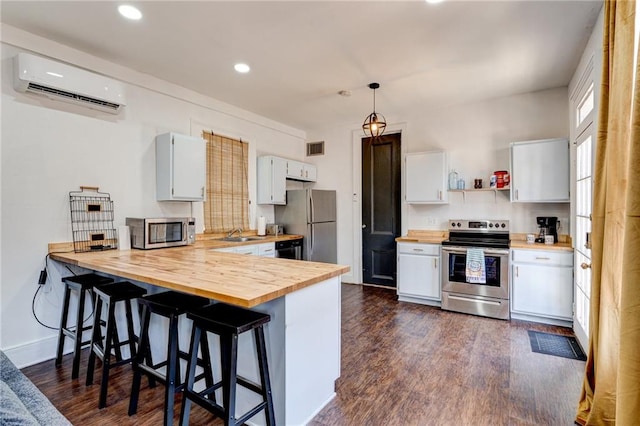 kitchen featuring a wall mounted air conditioner, white cabinetry, butcher block counters, and stainless steel appliances