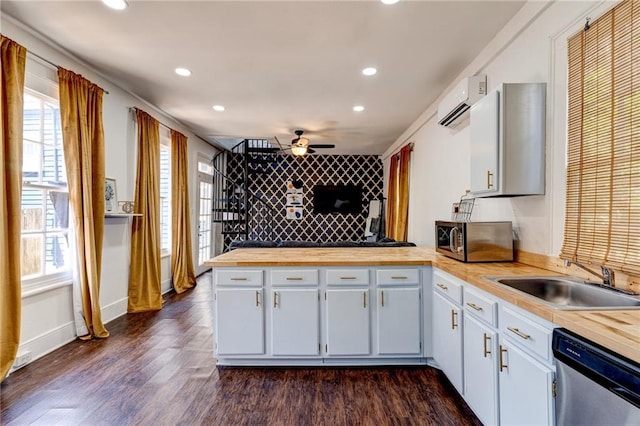 kitchen with kitchen peninsula, a wall unit AC, dark hardwood / wood-style flooring, appliances with stainless steel finishes, and sink