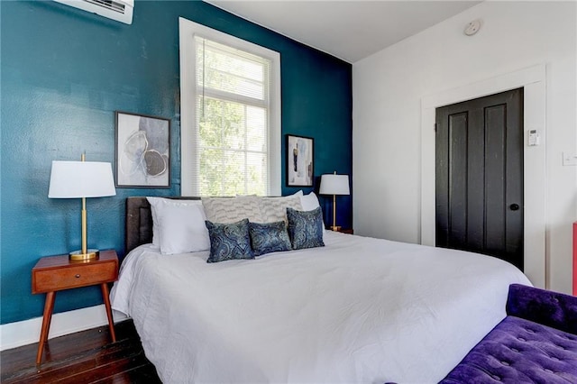 bedroom with dark hardwood / wood-style floors and an AC wall unit