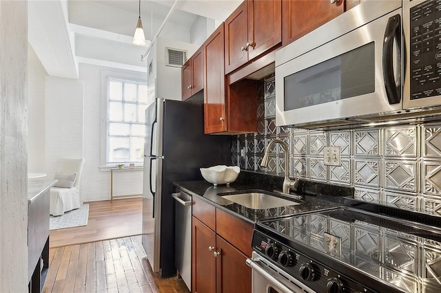 kitchen with sink, hanging light fixtures, dark stone counters, dark hardwood / wood-style flooring, and stainless steel appliances