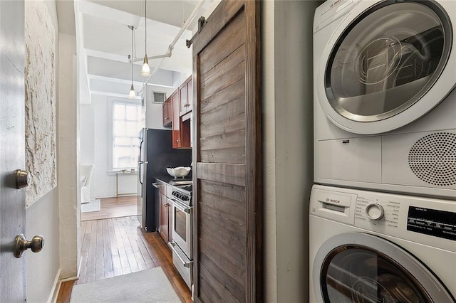 washroom featuring stacked washing maching and dryer, a barn door, and dark hardwood / wood-style floors