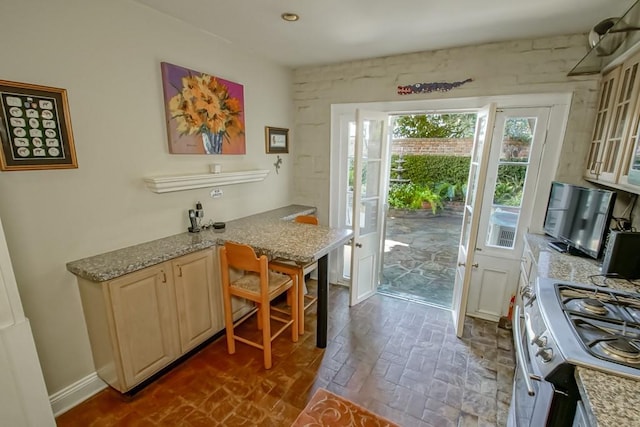 kitchen with light stone counters, stainless steel range oven, kitchen peninsula, and a kitchen breakfast bar