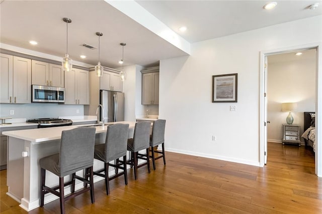 kitchen with appliances with stainless steel finishes, a center island with sink, dark hardwood / wood-style floors, and gray cabinetry