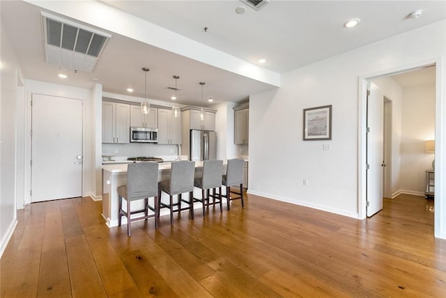 kitchen with a breakfast bar area, pendant lighting, stainless steel appliances, and hardwood / wood-style flooring