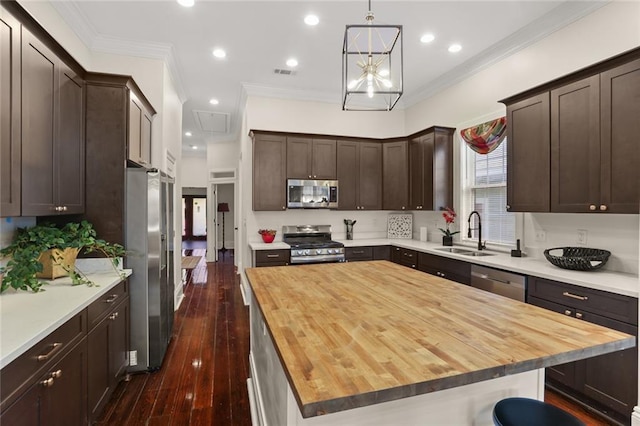 kitchen with butcher block countertops, a kitchen island, appliances with stainless steel finishes, hanging light fixtures, and sink