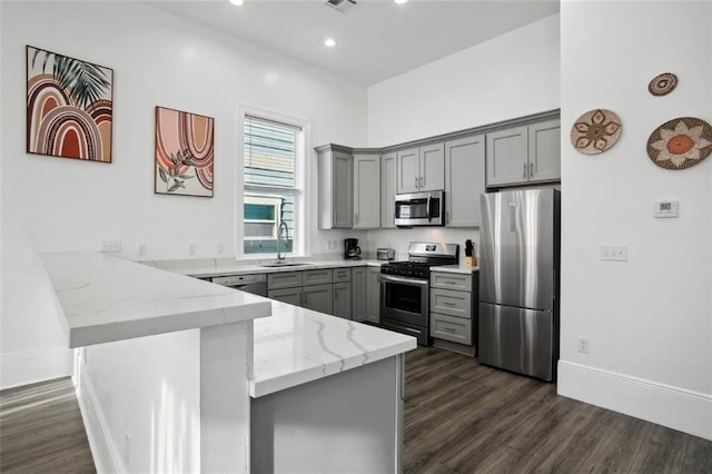 kitchen featuring sink, kitchen peninsula, light stone counters, appliances with stainless steel finishes, and dark hardwood / wood-style flooring