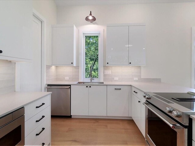 kitchen with sink, white cabinetry, light wood-type flooring, appliances with stainless steel finishes, and decorative backsplash