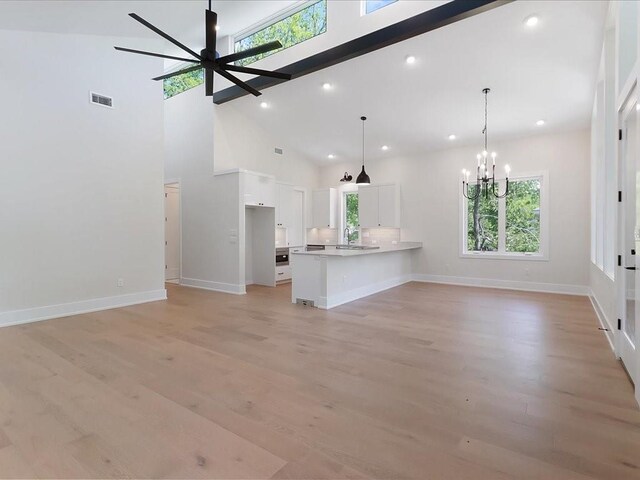 unfurnished living room with ceiling fan with notable chandelier, a wealth of natural light, high vaulted ceiling, and light wood-type flooring