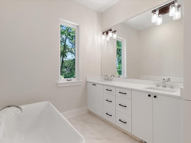 full bathroom with double vanity, marble finish floor, a freestanding tub, and a sink