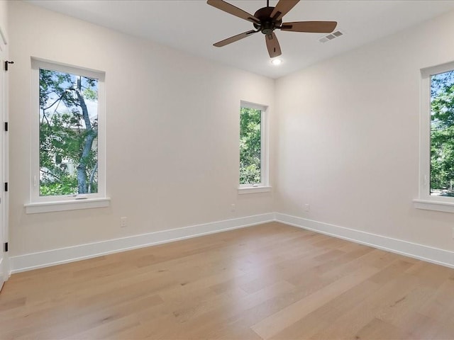 unfurnished room with a wealth of natural light, light wood-style flooring, visible vents, and baseboards