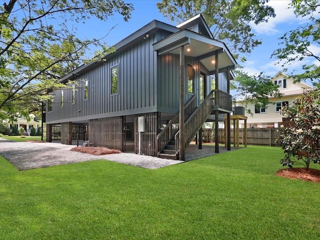 back of house with fence, stairway, board and batten siding, and a yard