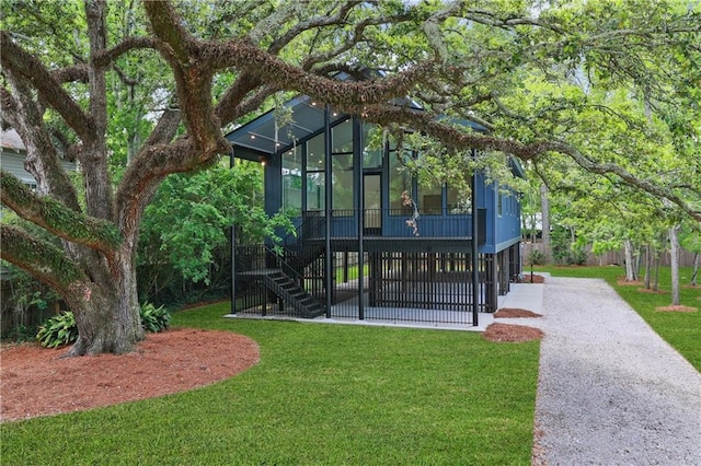 exterior space featuring driveway, a sunroom, stairs, and a yard