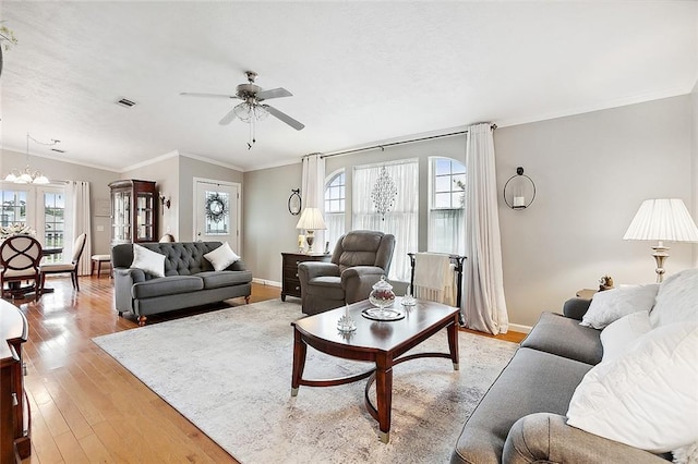 living room with a wealth of natural light, crown molding, ceiling fan with notable chandelier, and light hardwood / wood-style floors