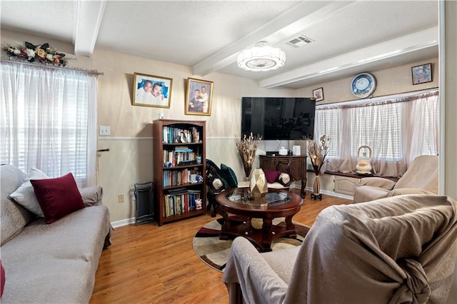 living room with a notable chandelier, beam ceiling, and light wood-type flooring