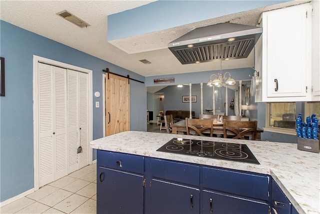 kitchen featuring black electric stovetop, wall chimney exhaust hood, a barn door, blue cabinetry, and white cabinets